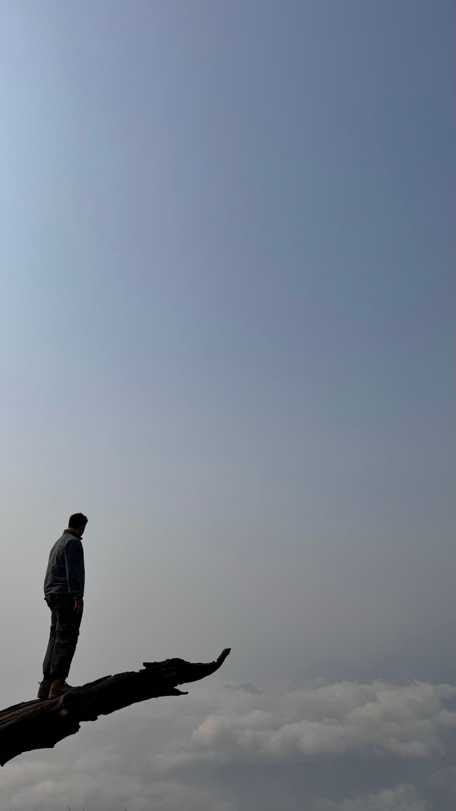 Lone figure on a rock above a sea of clouds in Y Tý