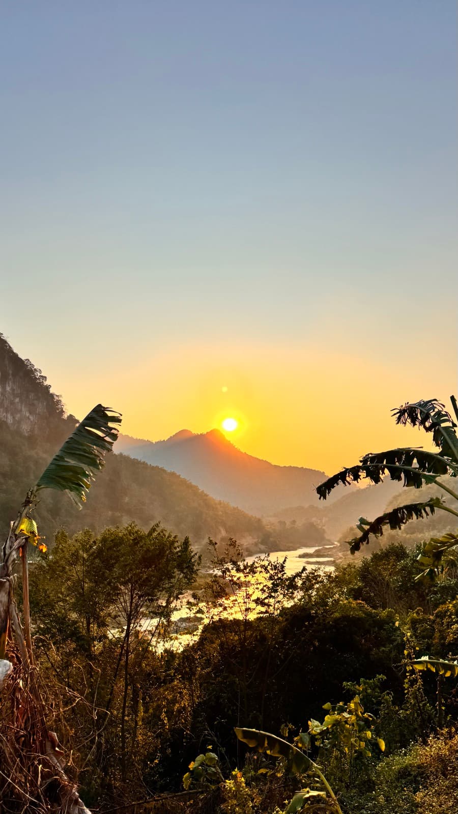 Golden sunset between the mountains framed by banana leaves