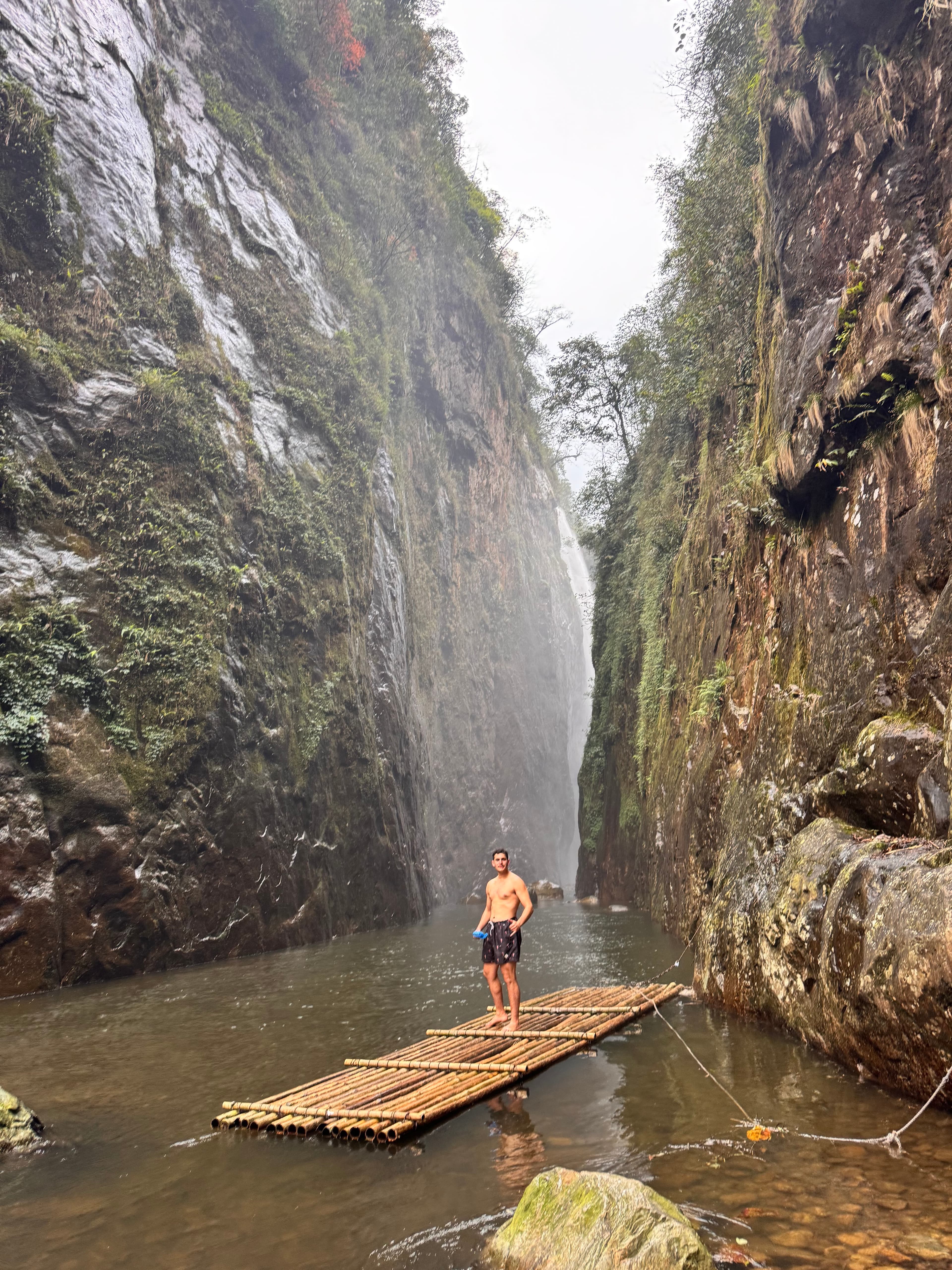 Standing on a bamboo raft in a towering hidden canyon near Mường Hum