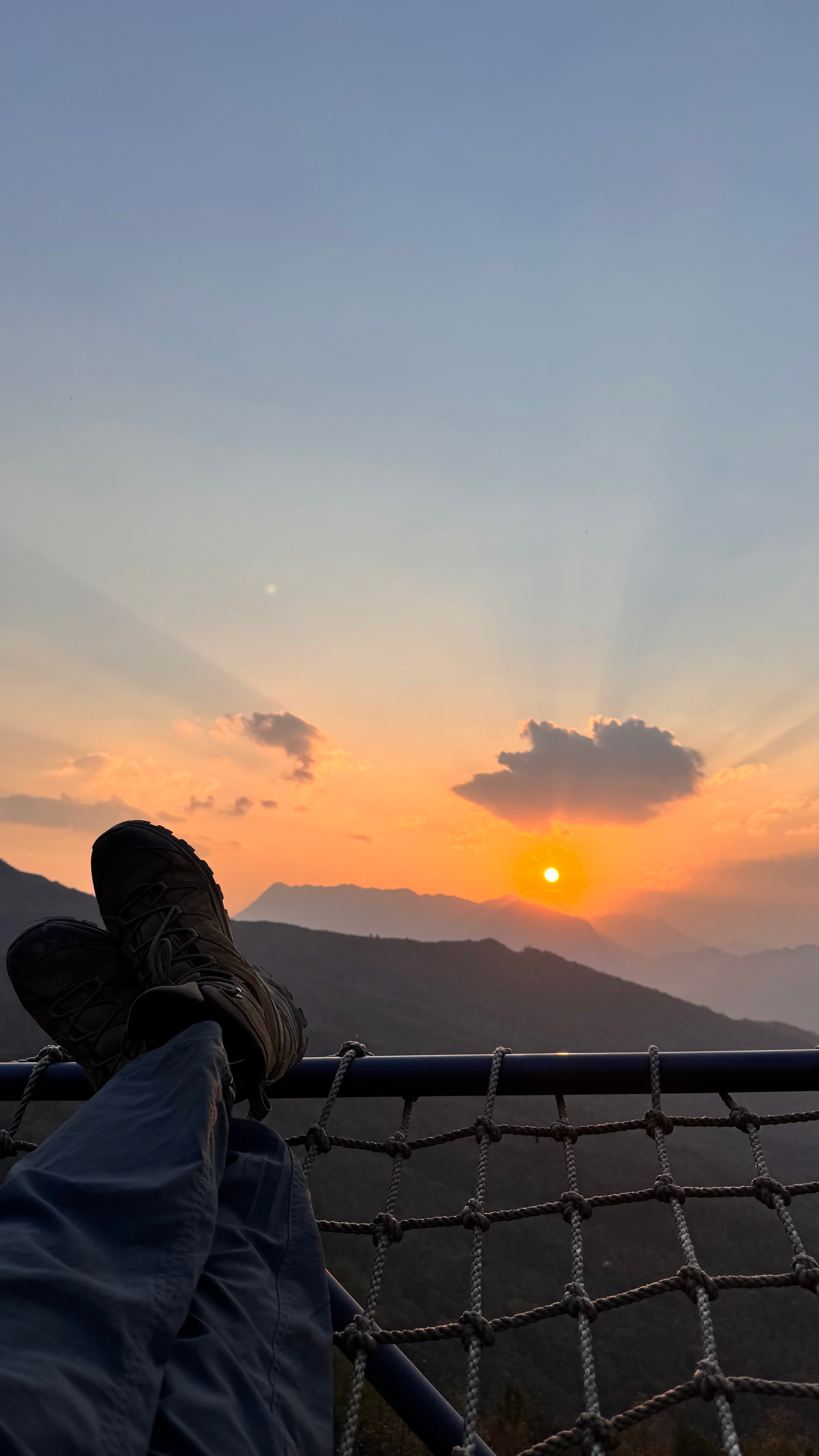 Feet up on a rope railing watching the sunset over the mountains in Y Tý