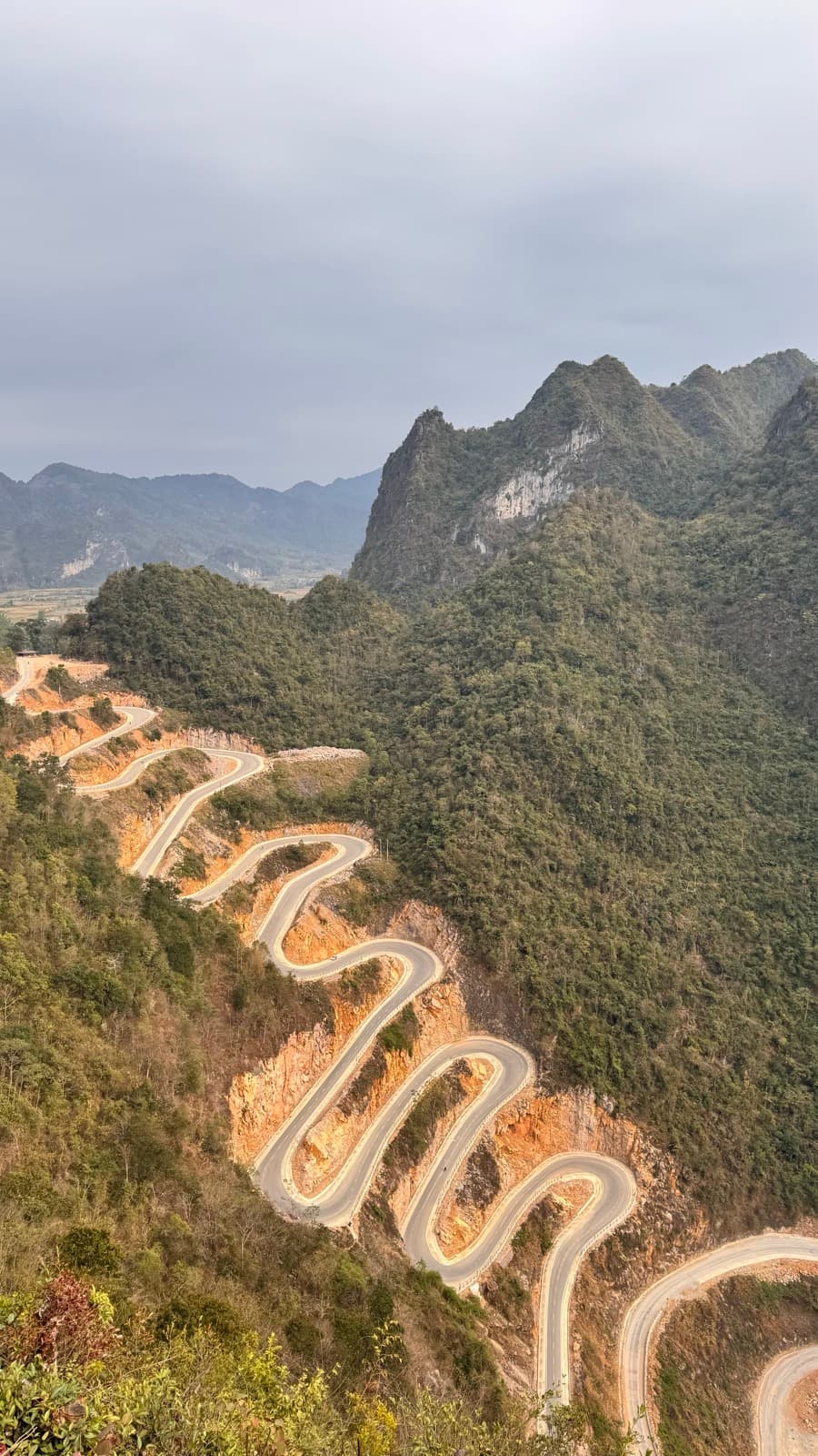 A winding mountain pass switchbacking down forested karst hills in Cao Bằng